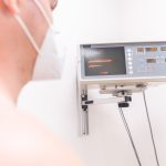 Paciente mascarado em uma clínica sendo monitorado por um equipamento eletrônico.
