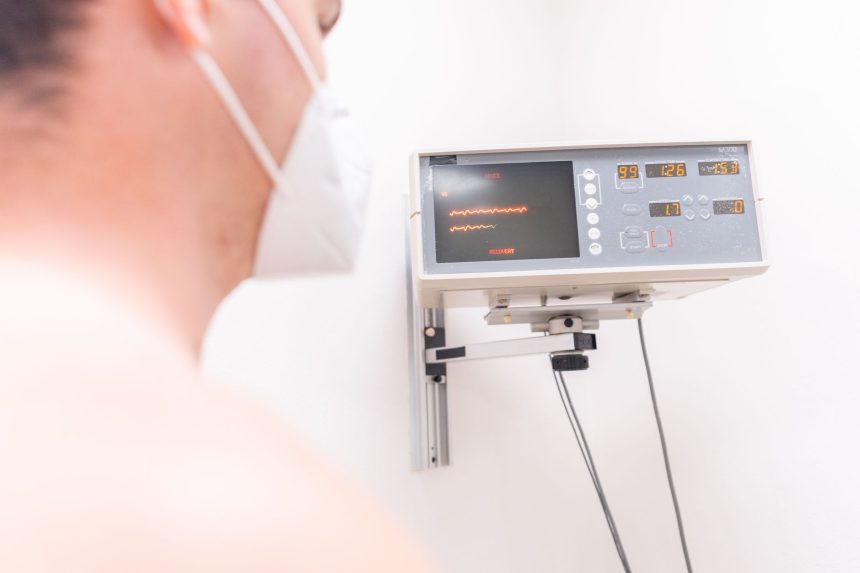 Paciente mascarado em uma clínica sendo monitorado por um equipamento eletrônico.