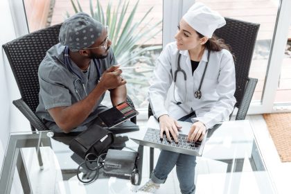 Dois médicos discutem cuidados de saúde usando um laptop e um tablet em ambiente clínico.